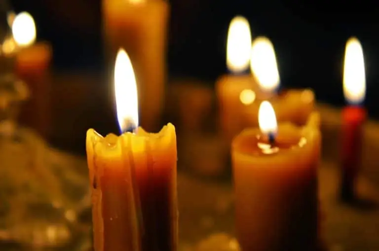 A group of candles burns brightly against a dark background, creating a warm and serene atmosphere. The wax drips down the sides of the candles, adding to the calming and cozy ambiance. The orange and yellow flames stand out vividly.