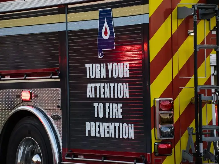 Close-up of the side of a fire truck displaying the message "Turn Your Attention to Fire Prevention" in large white letters, accompanied by an illustration of a water droplet. The truck features red and yellow diagonal stripes and reflective elements.